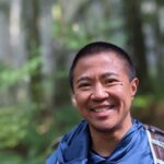 Man smiling in a forest with a backpack.