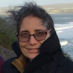 Woman wearing glasses smiles by the ocean.