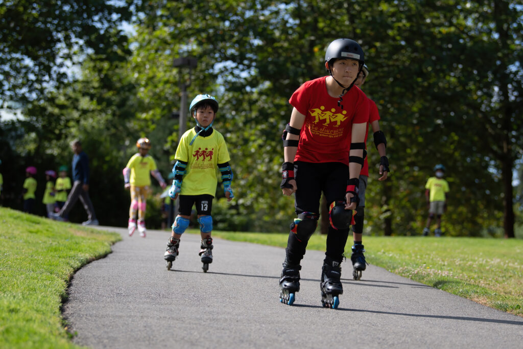 Children rollerblading on a path in a park.