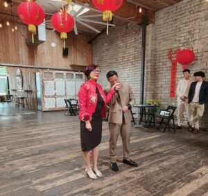 Woman in red jacket with man at wedding reception.