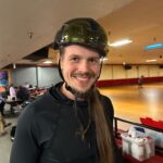 Man in black shirt and helmet at roller rink.