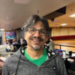 Smiling man wearing glasses and a hoodie.